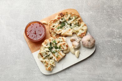 Photo of Delicious grilled cauliflower steaks with sauce and garlic on grey table, top view