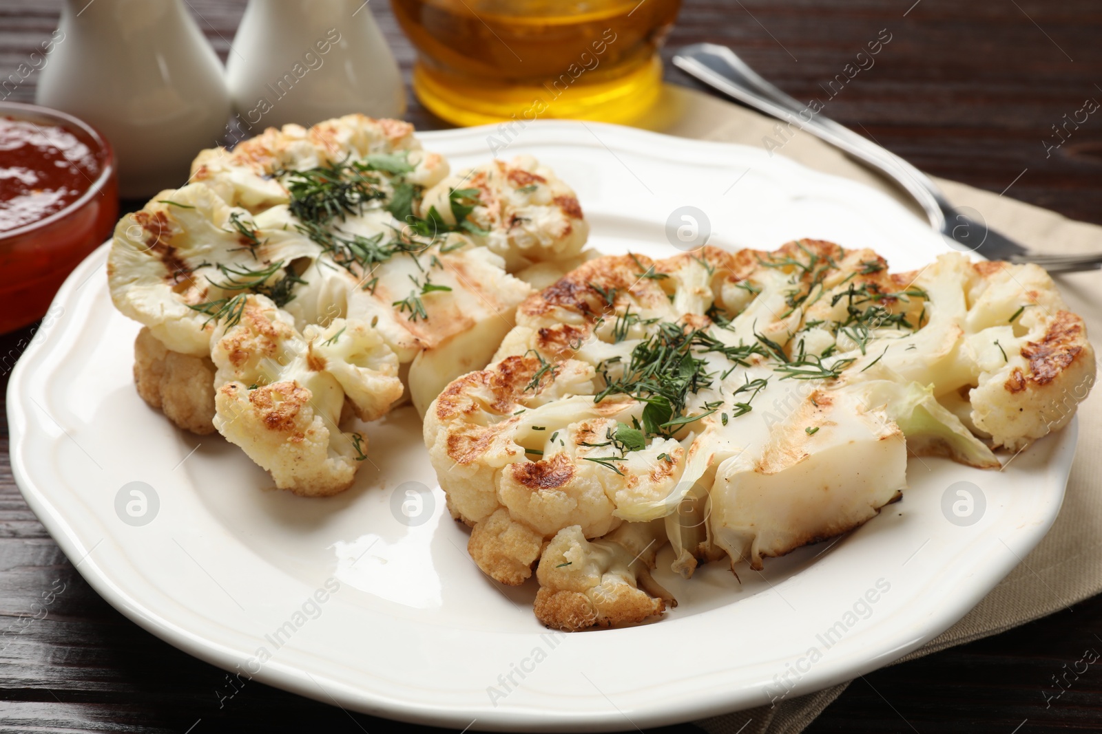 Photo of Delicious grilled cauliflower steaks with sauce and spices on wooden table, closeup