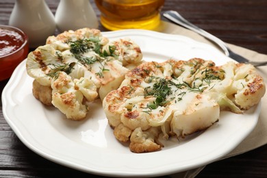 Photo of Delicious grilled cauliflower steaks with sauce and spices on wooden table, closeup