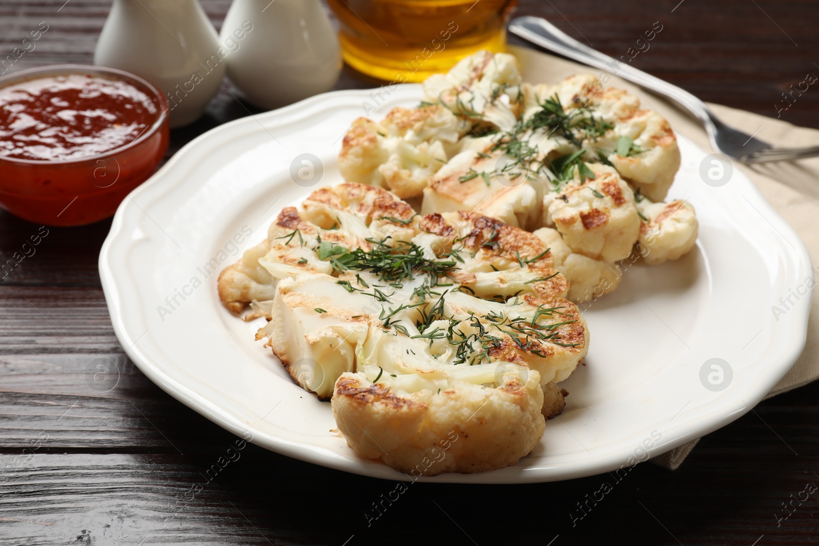 Photo of Delicious grilled cauliflower steaks with sauce and spices on wooden table, closeup