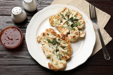 Photo of Delicious grilled cauliflower steaks with sauce and spices on wooden table, flat lay