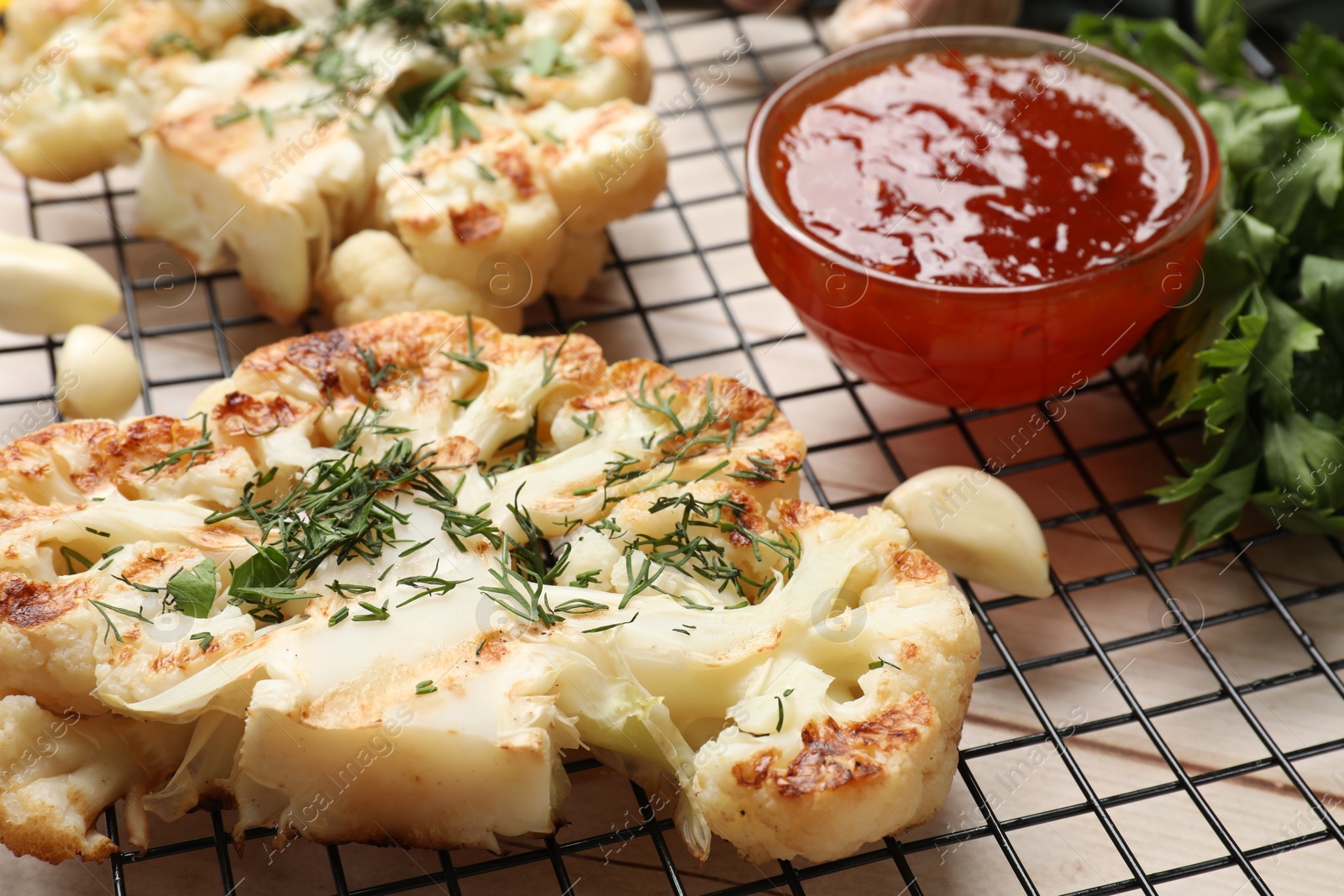 Photo of Delicious grilled cauliflower steaks with sauce and spices on wooden table, closeup