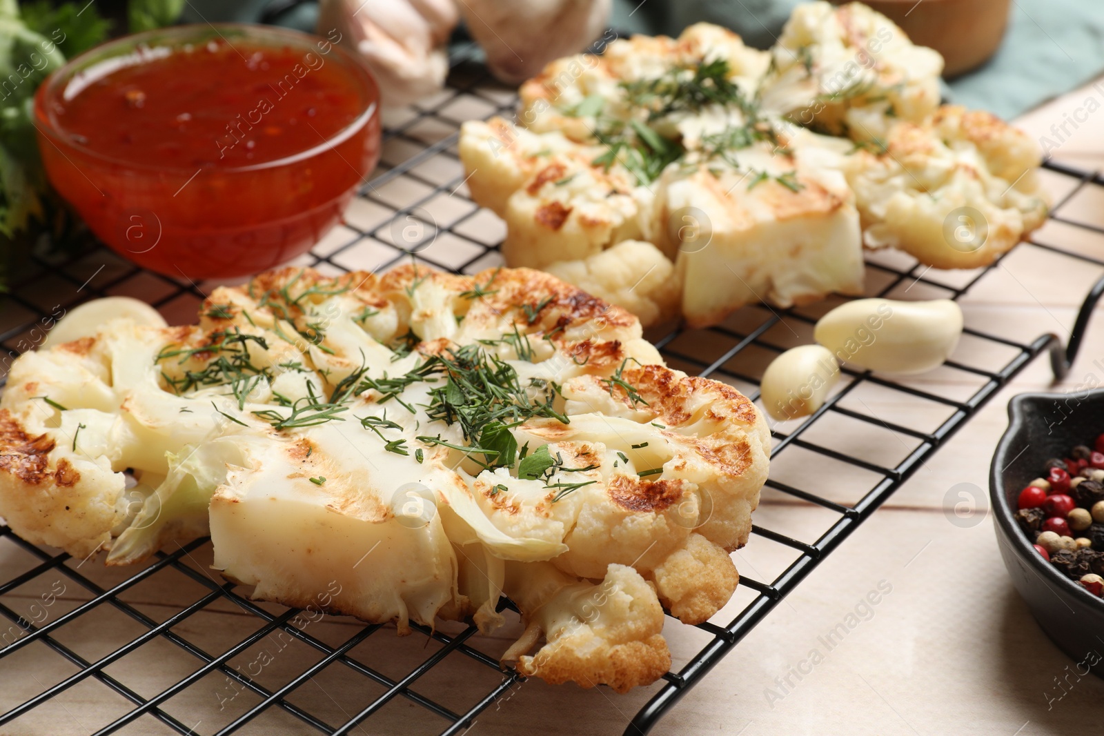 Photo of Delicious grilled cauliflower steaks with sauce and spices on wooden table, closeup