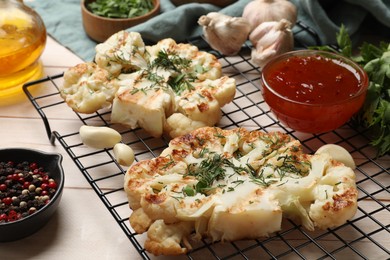 Photo of Delicious grilled cauliflower steaks with sauce and spices on wooden table, closeup