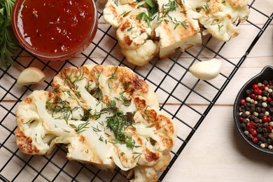 Photo of Delicious grilled cauliflower steaks with sauce and spices on wooden table, flat lay