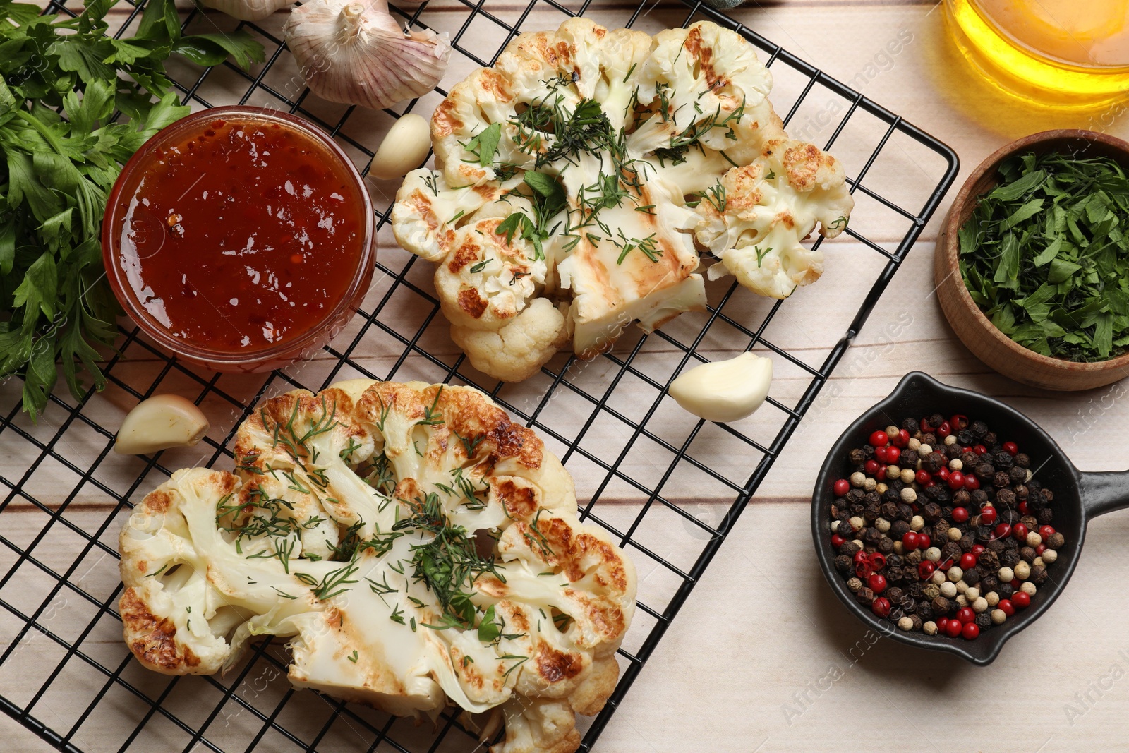 Photo of Delicious grilled cauliflower steaks with sauce and spices on wooden table, flat lay