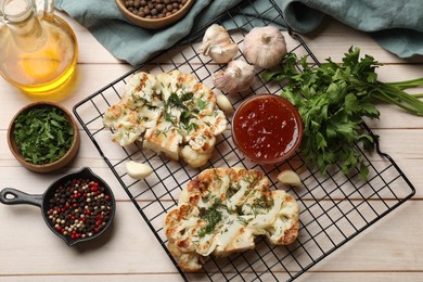 Photo of Delicious grilled cauliflower steaks with sauce and spices on wooden table, flat lay