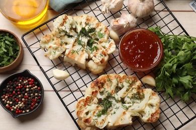 Delicious grilled cauliflower steaks with sauce and spices on wooden table, flat lay