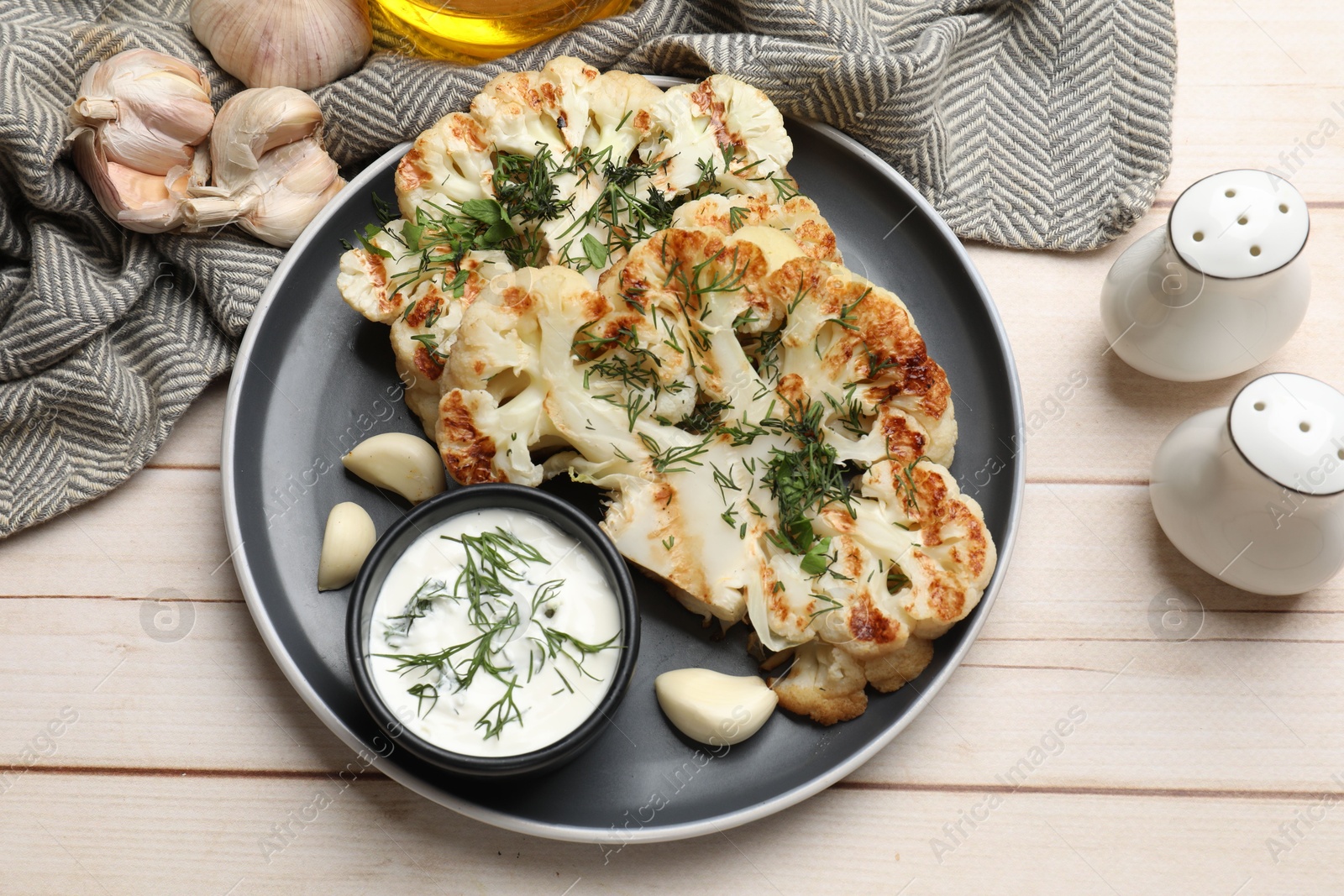 Photo of Delicious grilled cauliflower steaks with sauce, garlic and dill on wooden table, flat lay