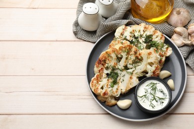 Photo of Delicious grilled cauliflower steaks with sauce, garlic and dill on wooden table, flat lay. Space for text