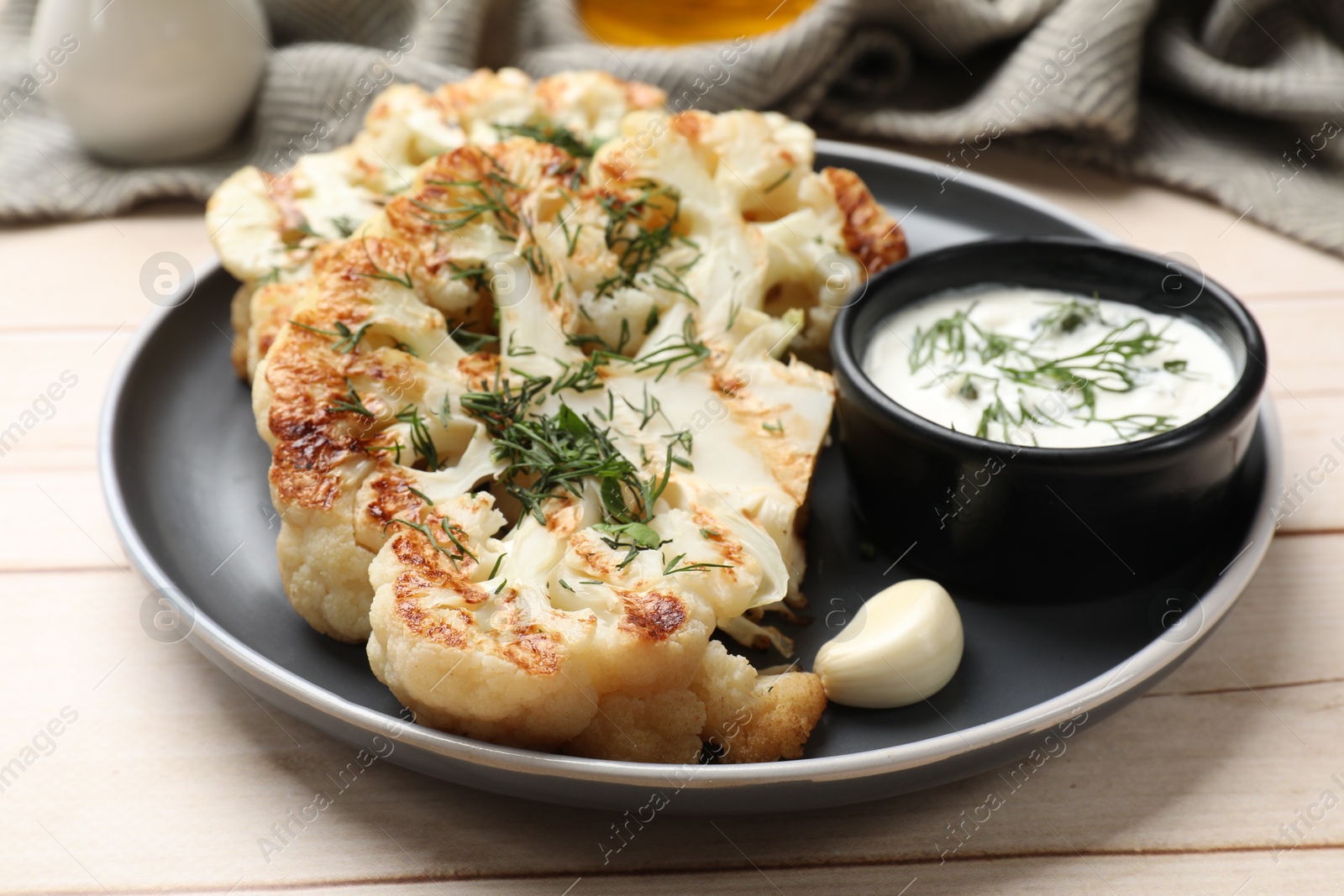 Photo of Delicious grilled cauliflower steaks with sauce, garlic and dill on wooden table