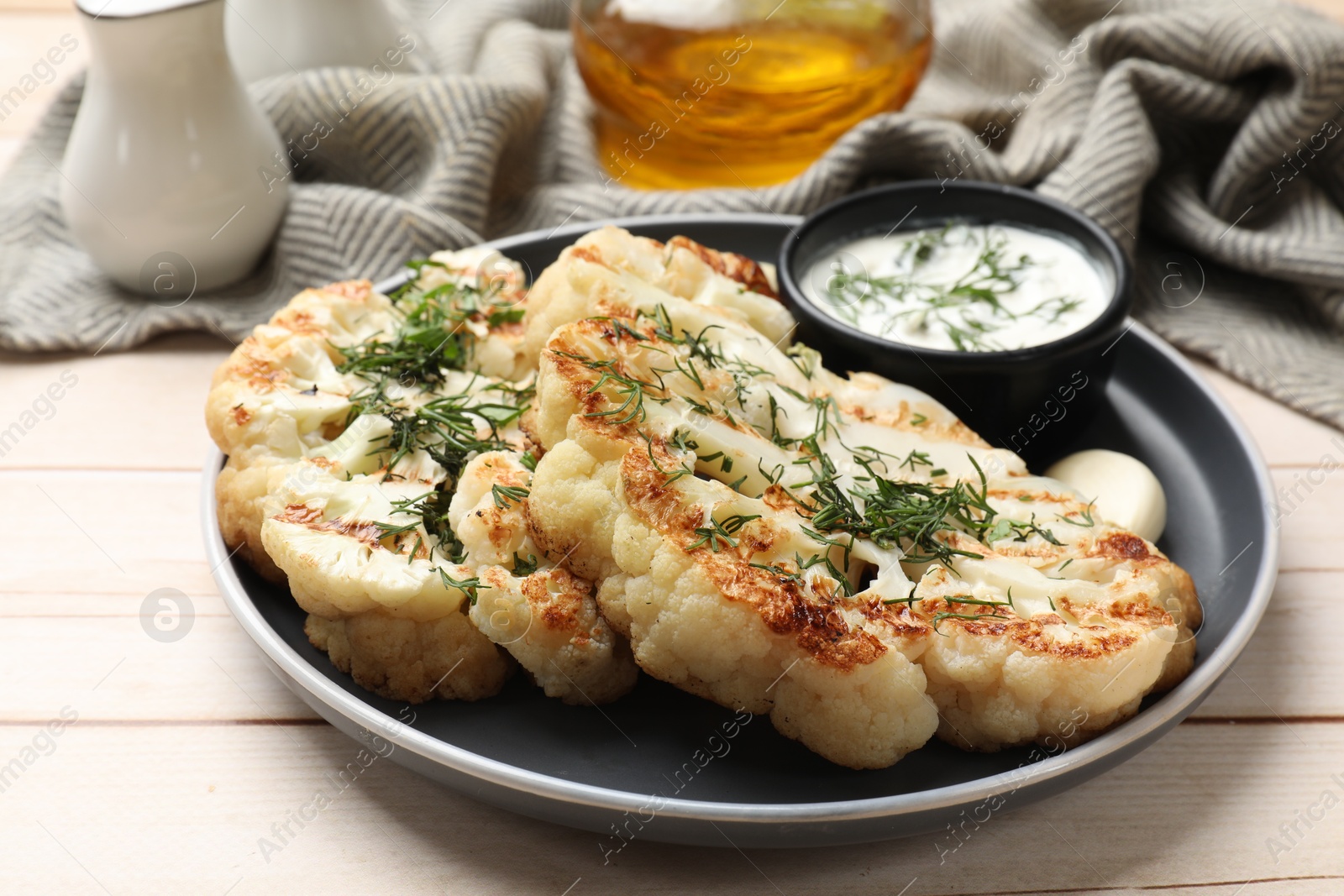 Delicious grilled cauliflower steaks with sauce, garlic and dill on wooden table Photo of Delicious grilled cauliflower steaks with sauce, garlic and dill on wooden table