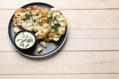 Photo of Delicious grilled cauliflower steaks with sauce, garlic and dill on wooden table, top view. Space for text