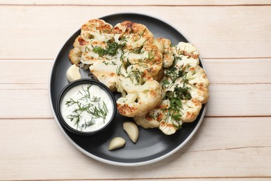 Photo of Delicious grilled cauliflower steaks with sauce, garlic and dill on wooden table, top view