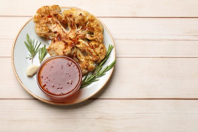 Photo of Delicious baked cauliflower steaks with sauce, garlic and rosemary on wooden table, top view. Space for text