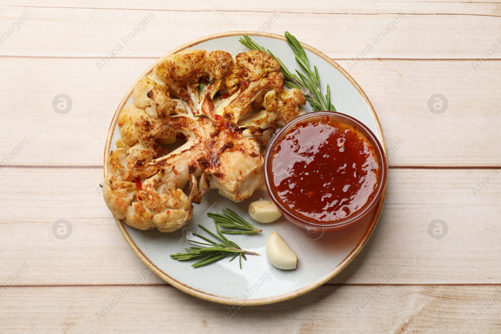 Photo of Delicious baked cauliflower steaks with sauce, garlic and rosemary on wooden table, top view