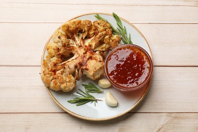 Delicious baked cauliflower steaks with sauce, garlic and rosemary on wooden table, top view