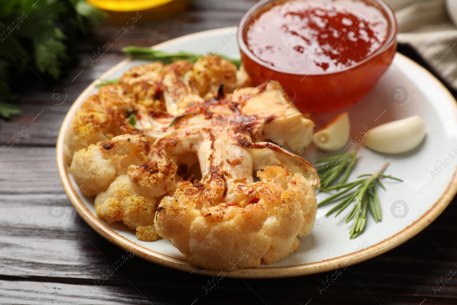 Photo of Delicious baked cauliflower steaks with sauce, garlic and rosemary on wooden table, closeup