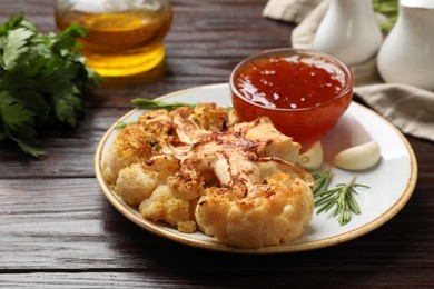 Photo of Delicious baked cauliflower steaks with sauce, garlic and rosemary on wooden table, closeup