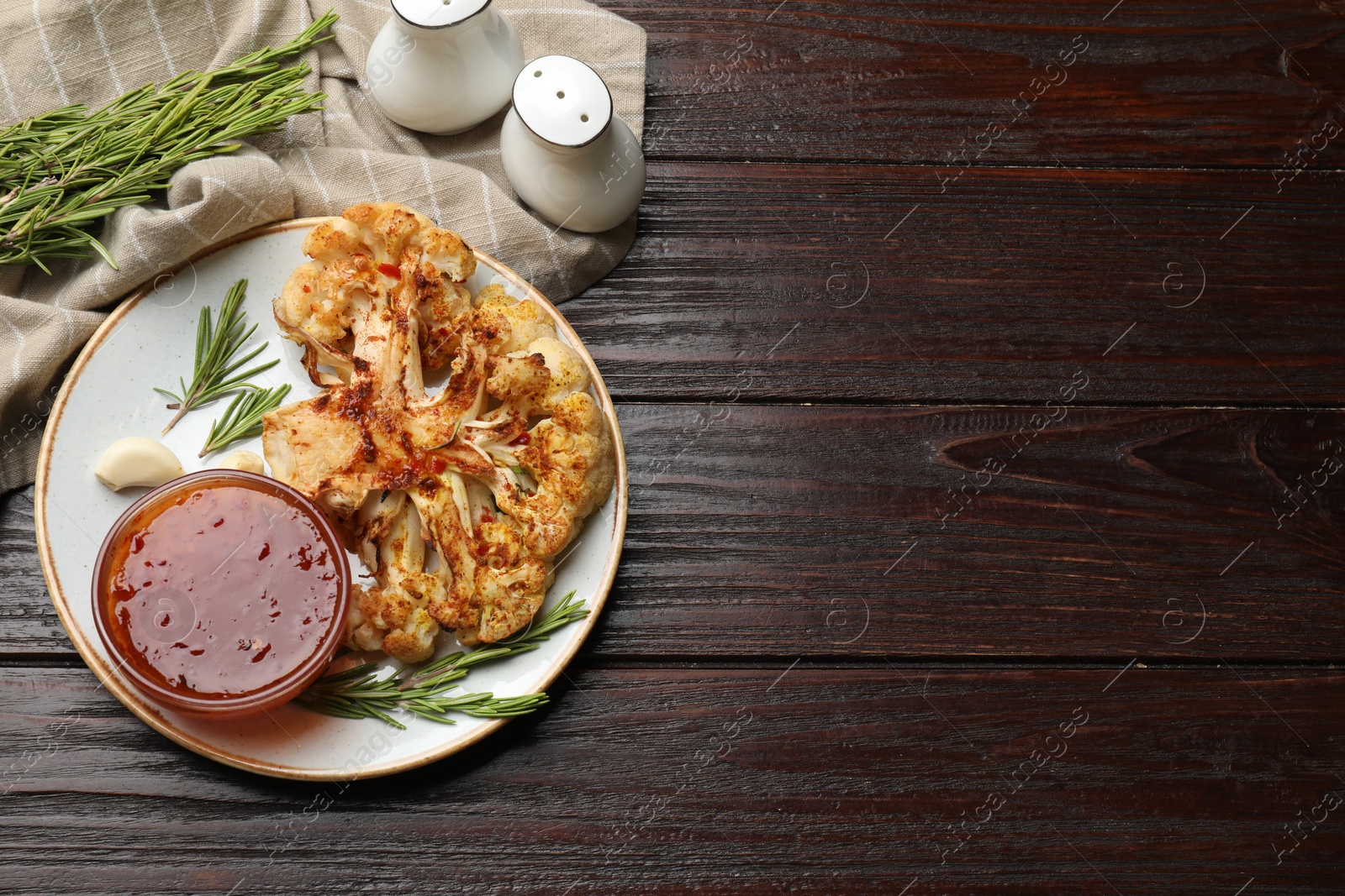 Photo of Delicious baked cauliflower steaks with sauce, garlic and rosemary on wooden table, flat lay. Space for text