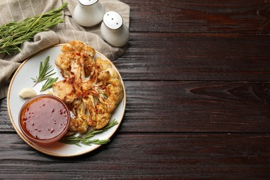 Photo of Delicious baked cauliflower steaks with sauce, garlic and rosemary on wooden table, flat lay. Space for text