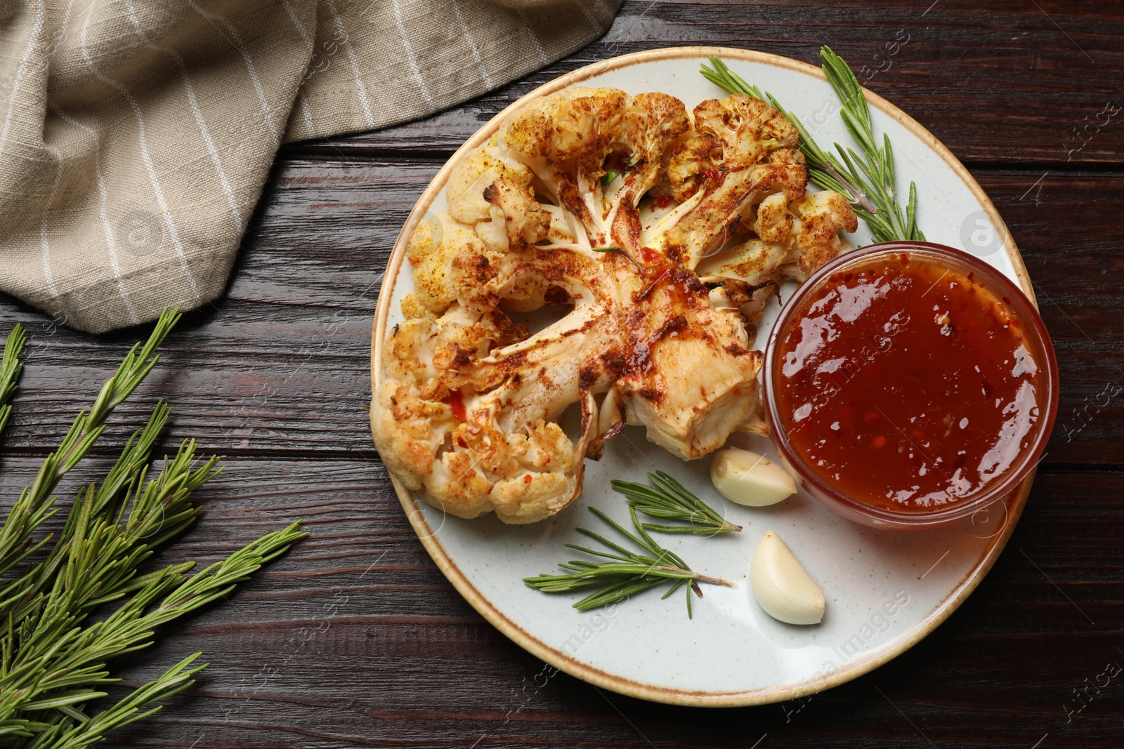 Photo of Delicious baked cauliflower steaks with sauce, garlic and rosemary on wooden table, flat lay