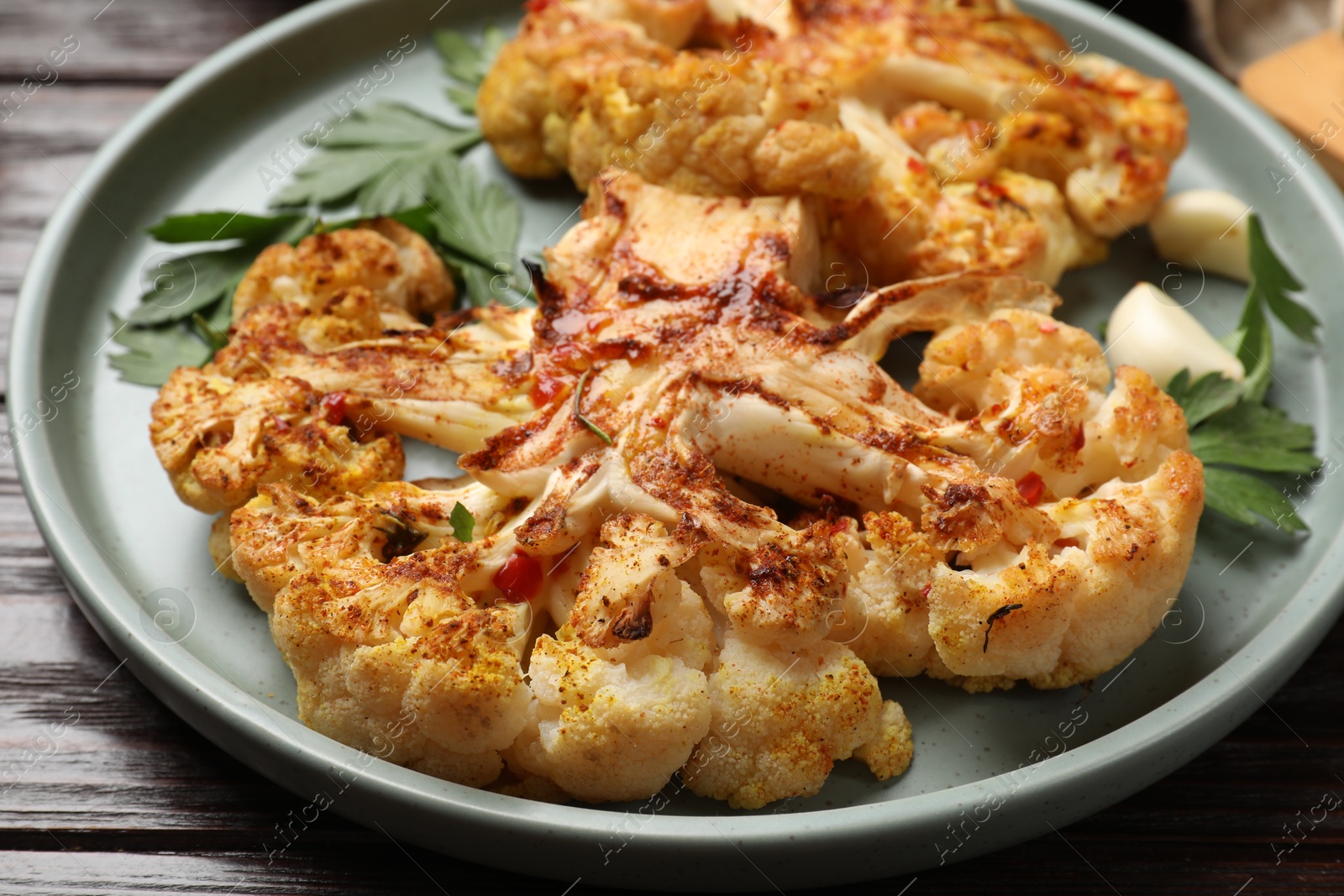 Photo of Delicious baked cauliflower steaks with garlic and parsley on wooden table, closeup