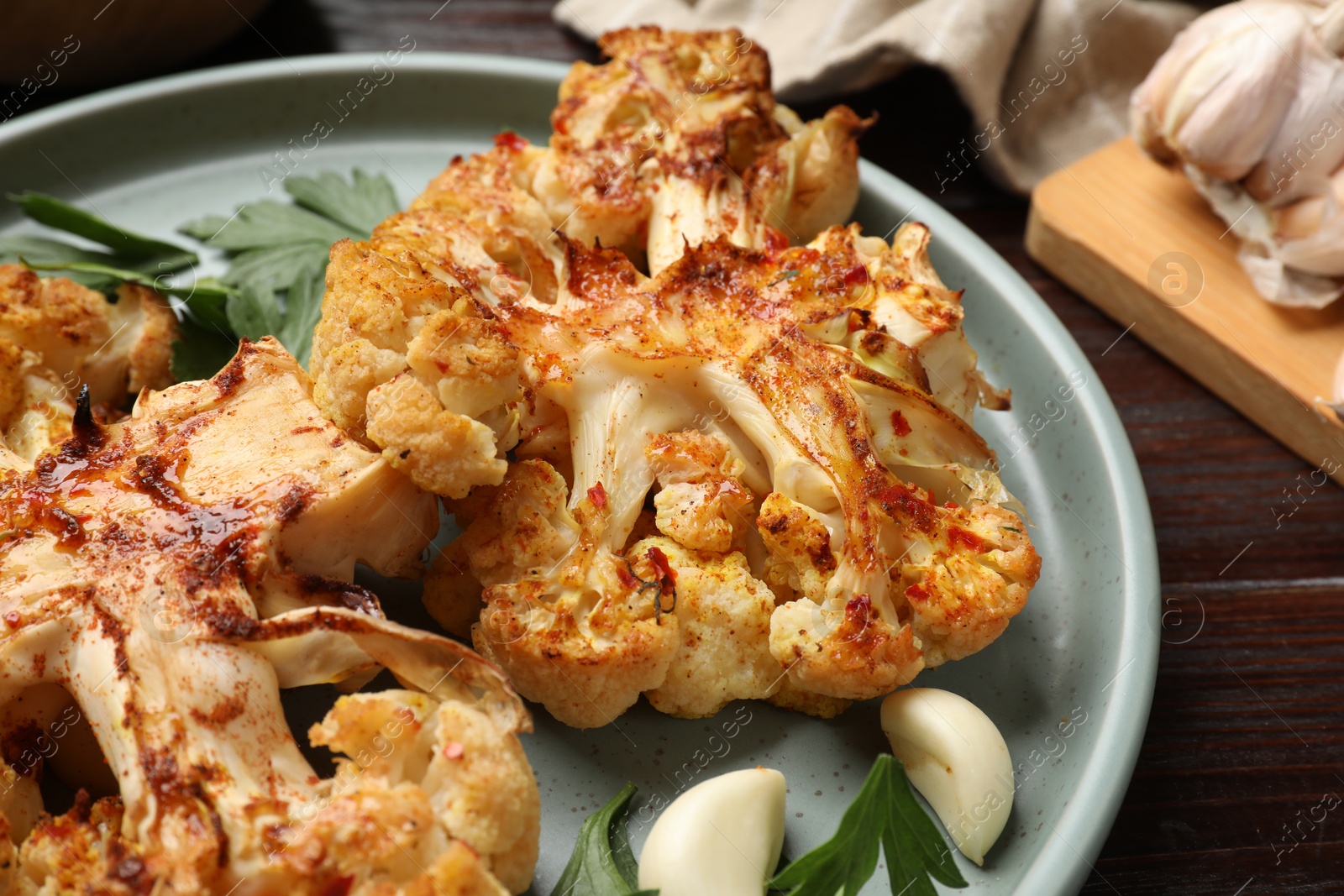 Photo of Delicious baked cauliflower steaks with garlic and parsley on wooden table, closeup