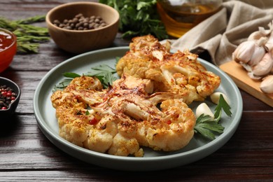 Photo of Delicious baked cauliflower steaks with garlic and parsley on wooden table, closeup