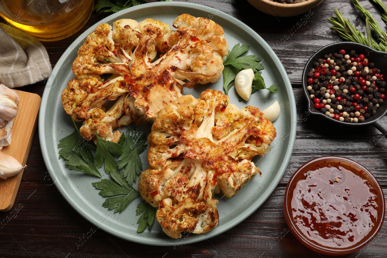 Photo of Delicious baked cauliflower steaks with sauce and spices on wooden table, flat lay