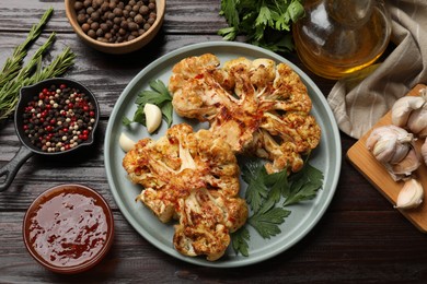 Photo of Delicious baked cauliflower steaks with sauce and spices on wooden table, flat lay