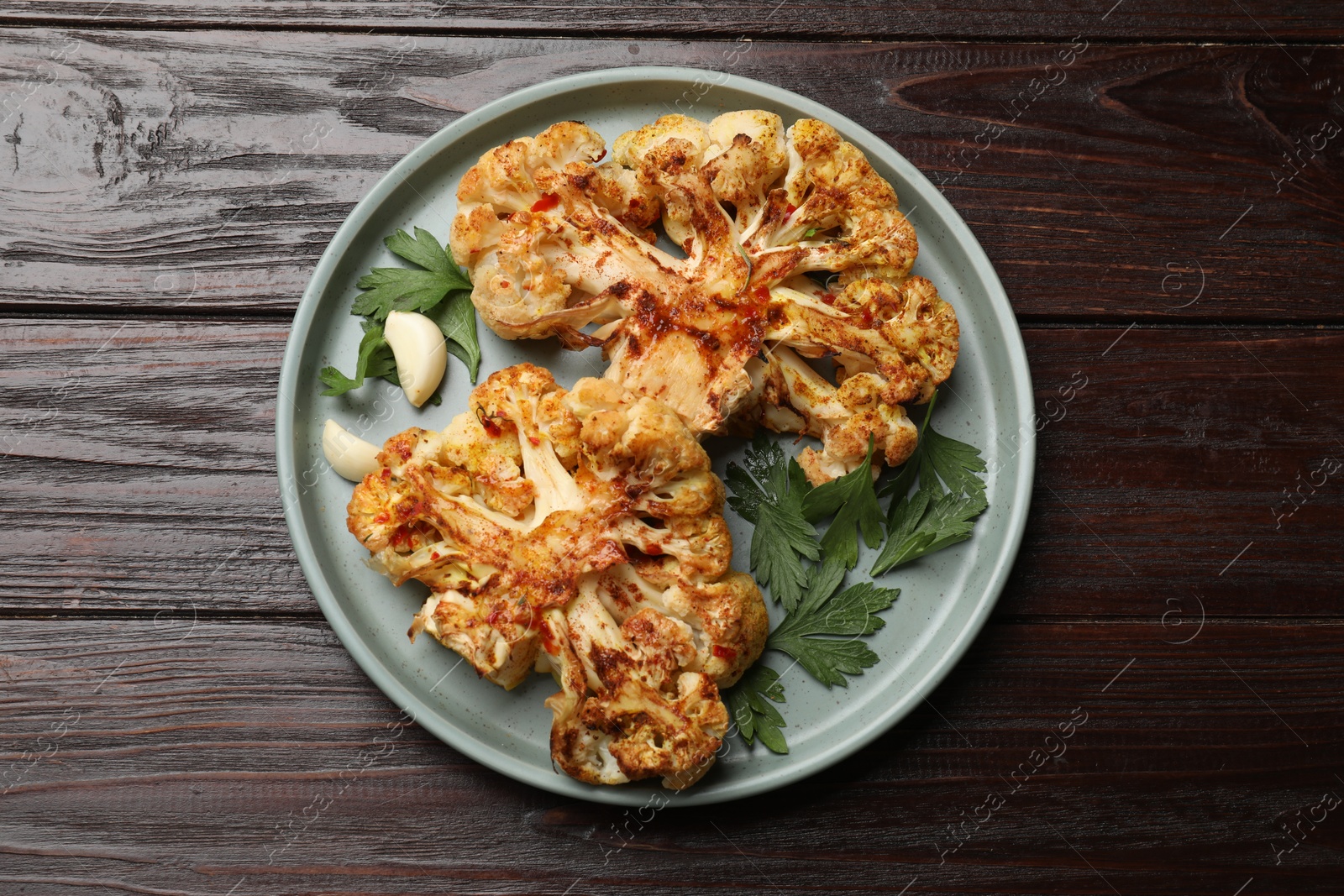 Photo of Delicious baked cauliflower steaks with garlic and parsley on wooden table, top view