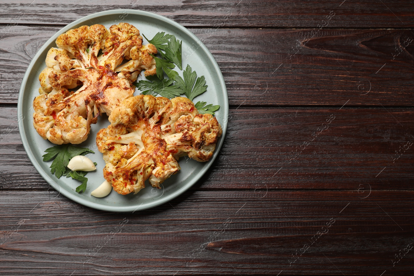 Photo of Delicious baked cauliflower steaks with garlic and parsley on wooden table, top view. Space for text