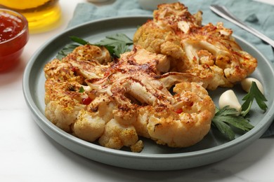 Delicious baked cauliflower steaks with garlic and parsley on white table, closeup