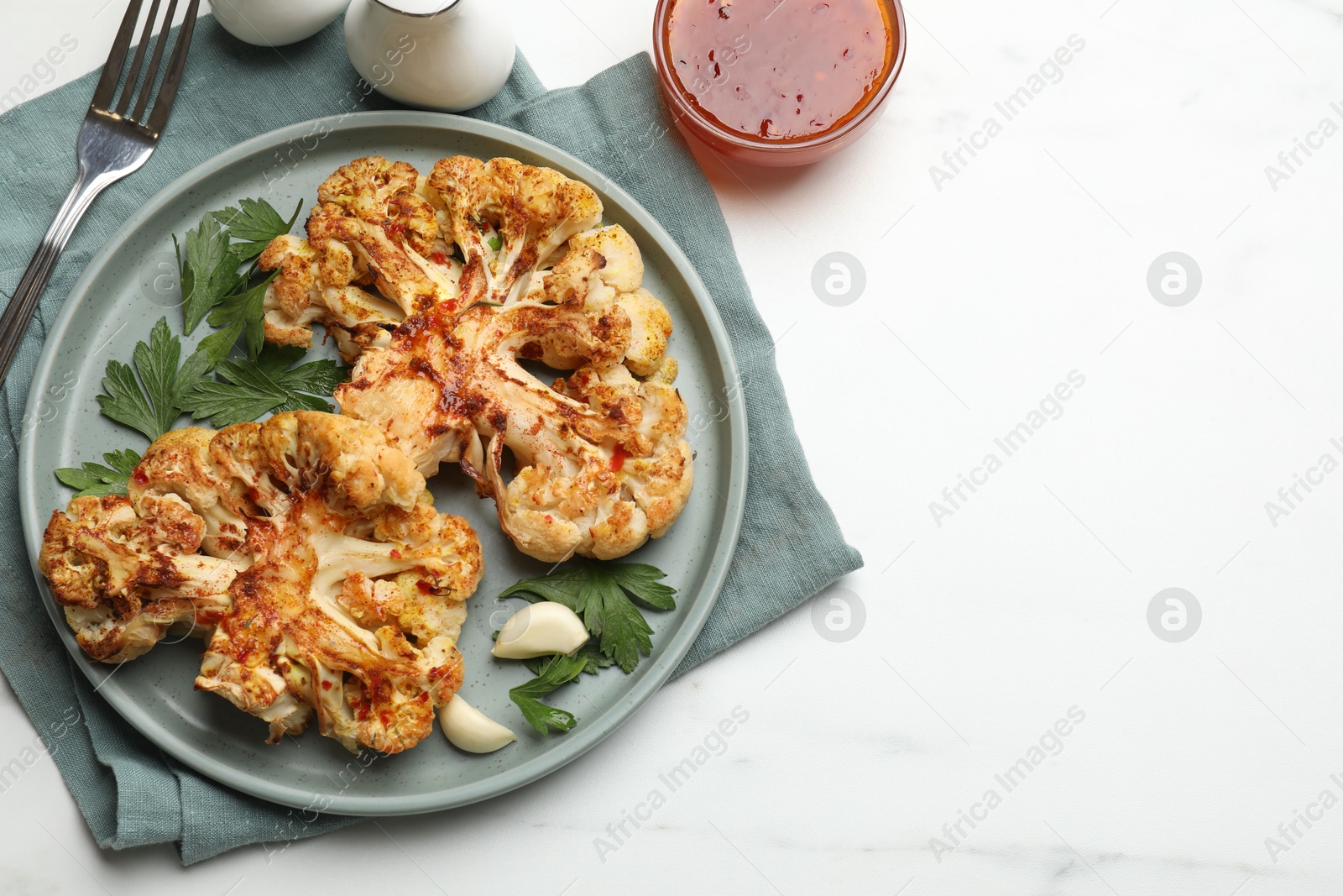 Photo of Delicious baked cauliflower steaks with garlic and parsley on white table, flat lay. Space for text