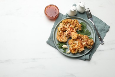 Photo of Delicious baked cauliflower steaks with garlic and parsley on white table, flat lay. Space for text