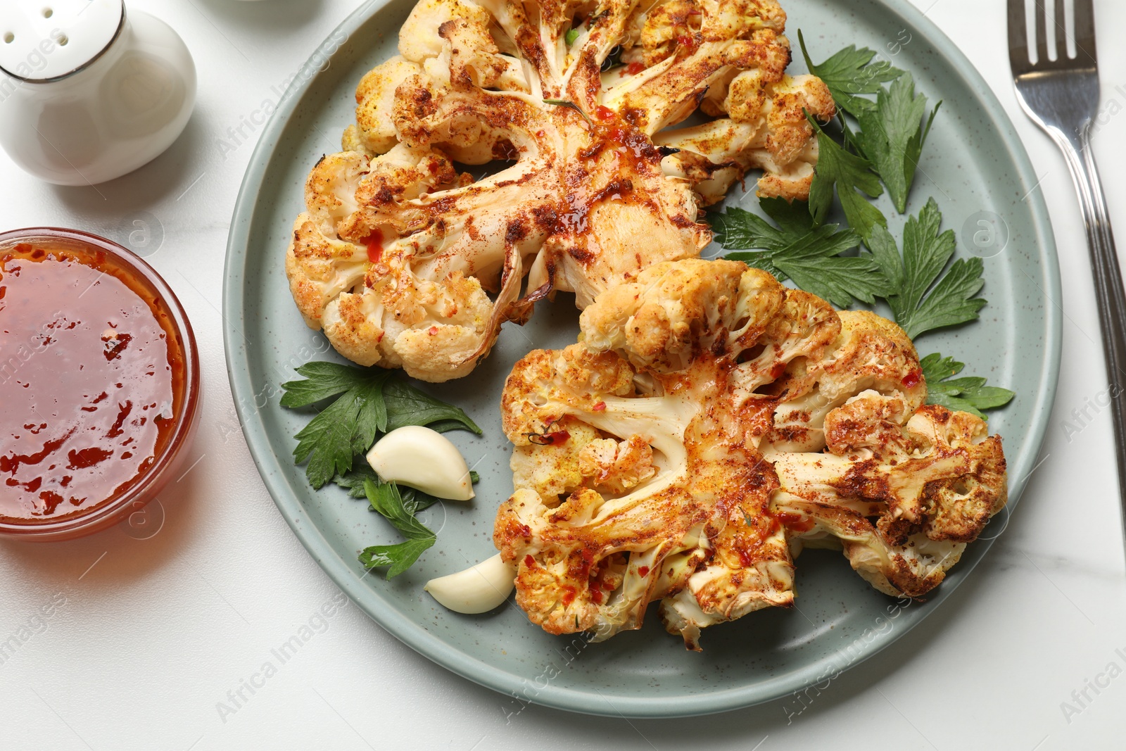 Photo of Delicious baked cauliflower steaks with garlic and parsley on white table, flat lay