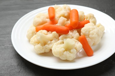 Photo of Tasty cauliflower with baby carrots on black table, closeup