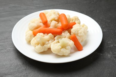 Photo of Tasty cauliflower with baby carrots on black table, closeup