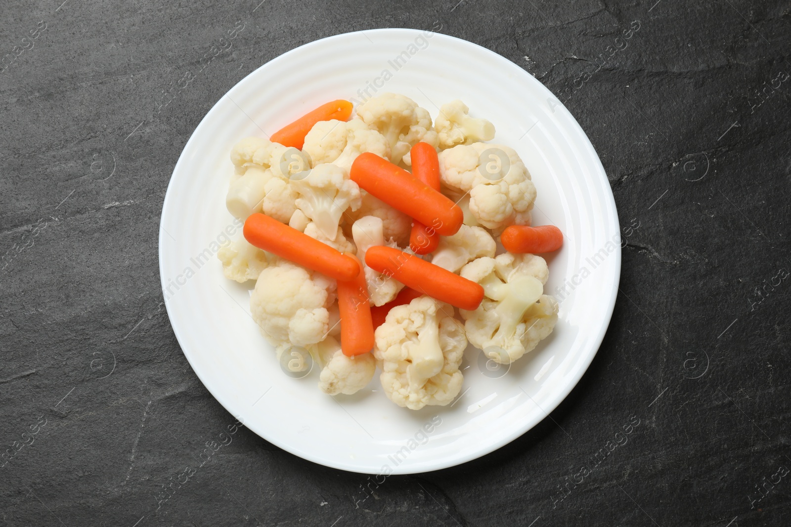 Photo of Tasty cauliflower with baby carrots on black table, top view