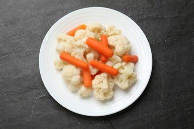 Photo of Tasty cauliflower with baby carrots on black table, top view