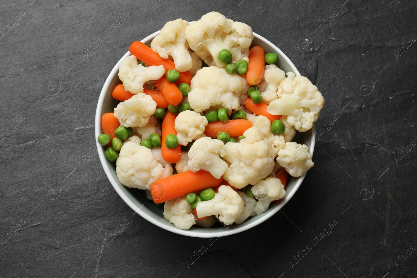 Photo of Tasty cauliflower with baby carrots and green peas on black table, top view