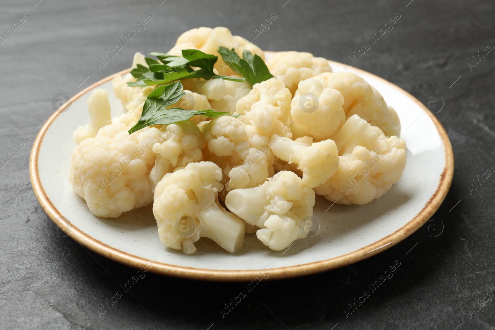 Photo of Tasty cauliflower with parsley on black table, closeup