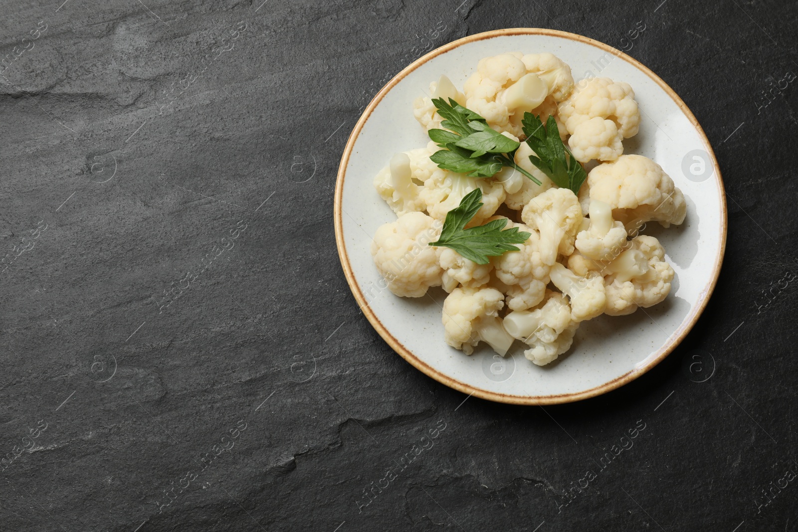 Photo of Tasty cauliflower with parsley on black table, top view. Space for text