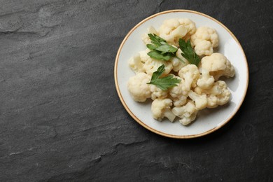 Photo of Tasty cauliflower with parsley on black table, top view. Space for text