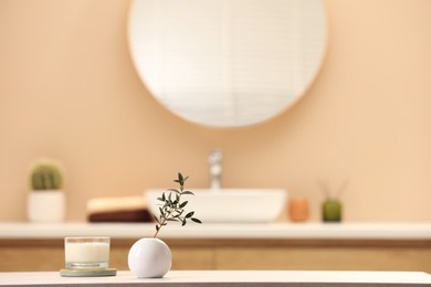 Photo of Scented candle and vase with green twig on table in bathroom. Space for text