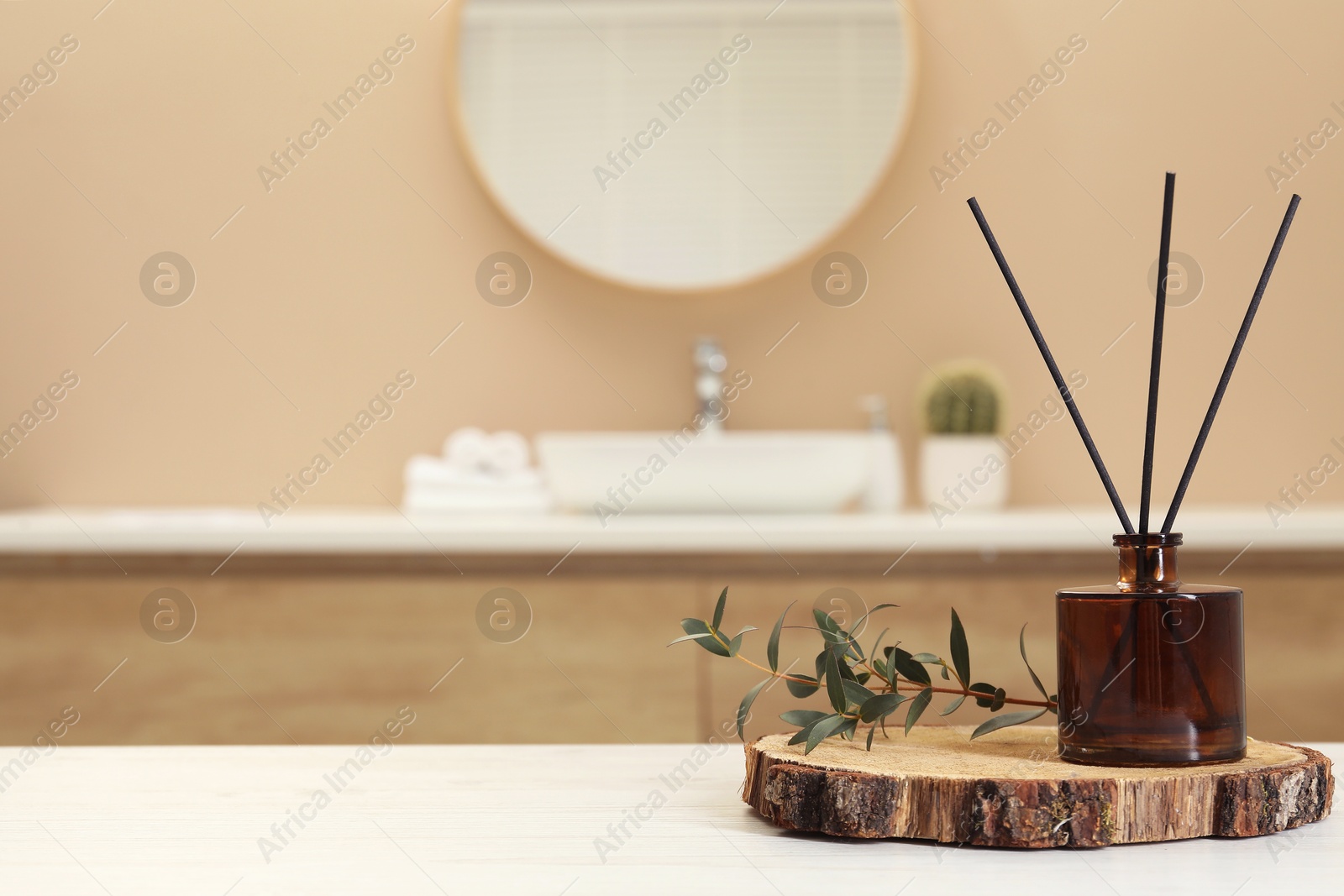 Photo of Reed diffuser and green twig on table in bathroom. Space for text