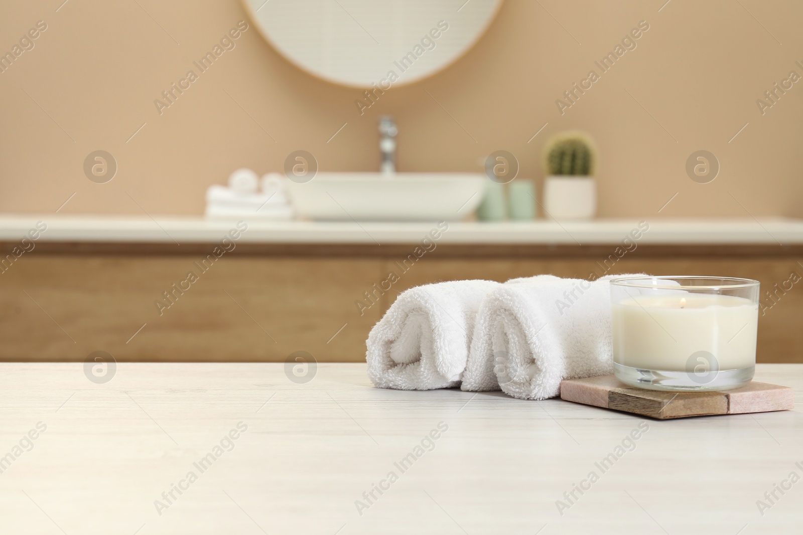 Photo of Scented candle and rolled towels on table in bathroom. Space for text