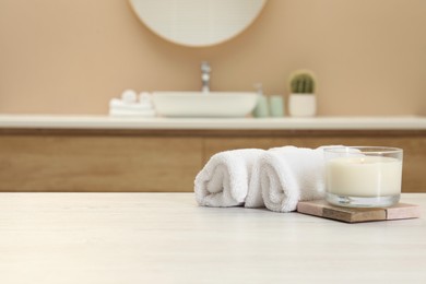 Scented candle and rolled towels on table in bathroom. Space for text