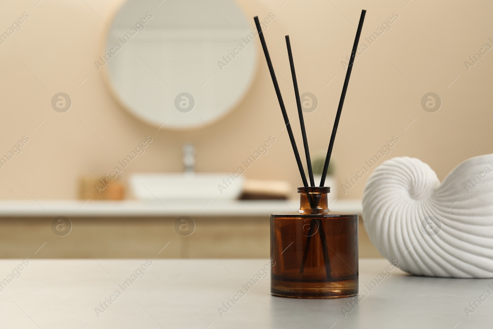 Photo of Reed diffuser and beautiful shell shaped vase on table in bathroom. Space for text